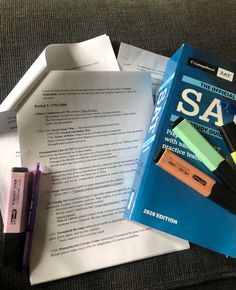 a pile of papers sitting on top of a couch next to a pen and marker