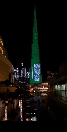 a tall building with lights on it's side at night in front of other buildings