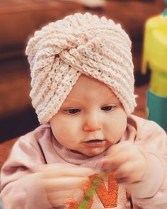 a baby wearing a knitted hat eating carrots