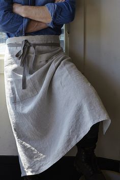 a man in an apron leaning on a window sill with his arms crossed and looking at the camera