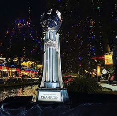 a giant trophy sitting in the middle of a river at night with people walking around it