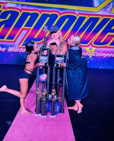 three women standing around a trophy on top of a pink carpet