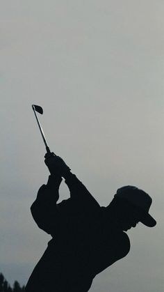 the silhouette of a man holding a golf club in front of his head and wearing a hat