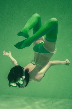 a woman in green swimsuit diving under water with her legs spread out to the side