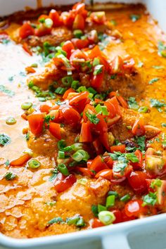 a casserole dish with meat, tomatoes and green onion garnishes