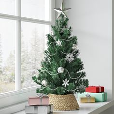 a small christmas tree sitting on top of a white table next to presents and a window