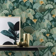 a gold vase sitting on top of a table next to a green wallpaper covered in leaves