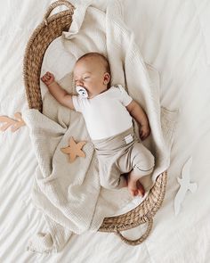 a baby is sleeping in a basket on a white blanket with an animal shaped pacifier