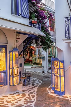 an alley way with tables and chairs in front of the storefronts, lit up at night