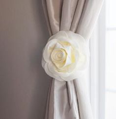 a white rose is on the corner of a window with drapes and draperies