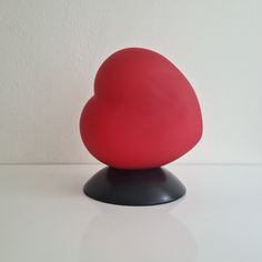 a red heart shaped object sitting on top of a black stand next to a white wall