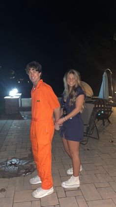 two people in orange jumpsuits standing next to each other on a brick patio