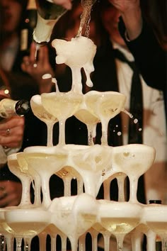 champagne being poured into wine glasses on top of a table with people standing around it