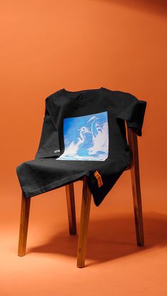 a black t - shirt sitting on top of a wooden chair with an orange background