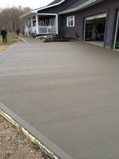 a concrete driveway being built in front of a house with two people walking by it