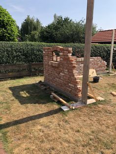 a brick oven in the middle of a yard next to a wooden pole and fence