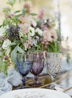 three wine glasses sitting on top of a table next to a vase filled with flowers