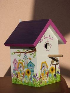 a birdhouse with flowers painted on the side and purple roof is sitting on a table