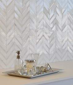 a tray that has some bottles on it next to a wall with white chevron tiles