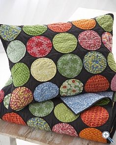 two pillows sitting on top of a wooden bench next to each other with different colored circles