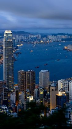 the city skyline is lit up at night with boats in the water and skyscrapers on both sides