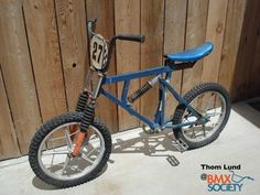 a small blue bike parked next to a wooden fence with a number on the front tire