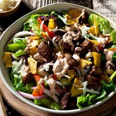 a salad with dressing in a bowl on a wooden table next to a fork and spoon