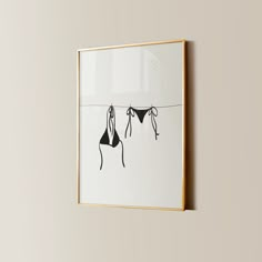 two bikinis hanging on a line in front of a wall with a gold frame