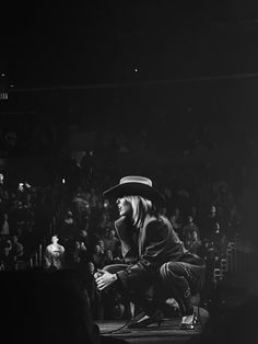 a person kneeling down in front of a crowd at a concert wearing a cowboy hat