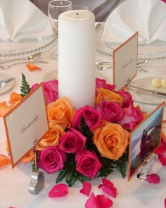 an arrangement of flowers and candles on a table with place settings for the guests to sit at