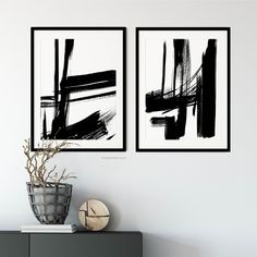 two black and white paintings hanging on the wall next to a vase filled with flowers