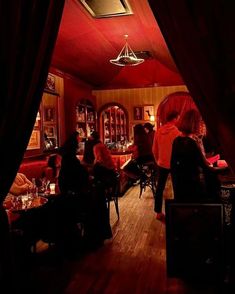 people sitting at tables in a dimly lit room with red walls and wood flooring