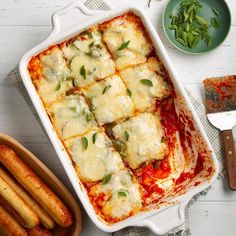 a casserole dish filled with meat and cheese next to some breadsticks