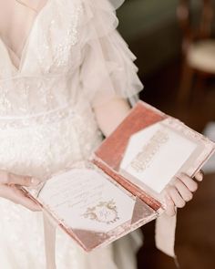 a woman in a white dress holding an open box with two wedding cards on it