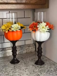 two vases with flowers in them sitting on a counter