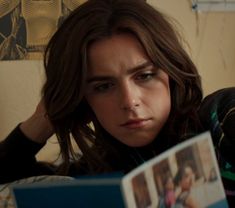 a woman is reading a book while sitting on the couch with her head resting on her hand