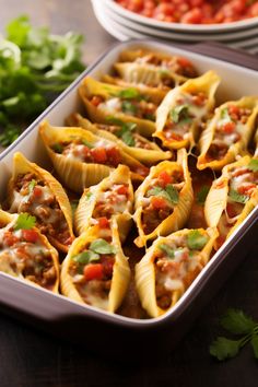 some taco shells are in a pan on a table next to tomatoes and cilantro