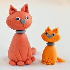 two clay cats sitting next to each other on a white surface with one cat looking at the camera