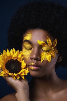 a woman with sunflowers painted on her face is holding a flower in front of her face