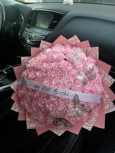 a bouquet of pink roses sitting in the front seat of a car with a happy birthday ribbon on it