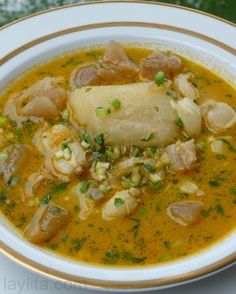 a white bowl filled with soup and meat on top of a table next to a green leafy plant