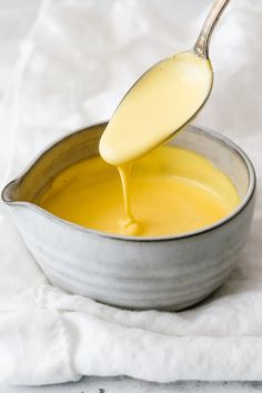 a spoon full of yellow liquid being poured into a bowl with white cloth on the side