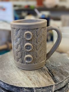 a coffee cup with buttons on it sitting on top of a wooden table next to other items