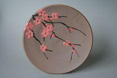 a plate with pink flowers painted on the side and black stems in the middle, sitting on a gray surface