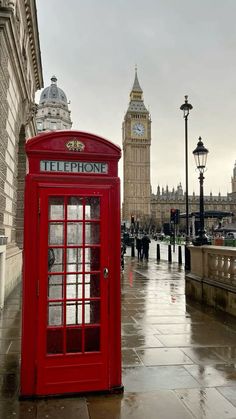 a red phone booth sitting on the side of a street next to a clock tower