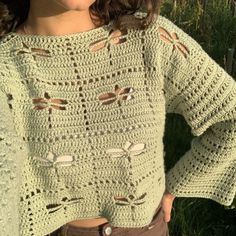 a woman standing in the grass with her hands on her hips wearing a green crocheted sweater