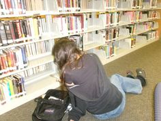 a woman sitting on the floor in front of a book shelf filled with books and backpacks