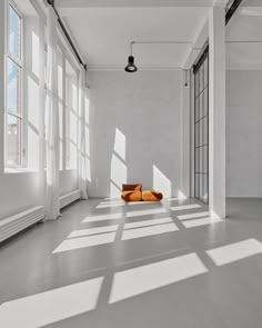 Sunlight streaming into a minimalist studio space with white walls and an orange seat, highlighting the large sliding glass door. Loft Photo Studio, Minimal Set Design, Garage Photography Studio, Minimalism Photography, Creative Studio Space