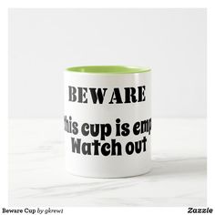 a white and green coffee mug sitting on top of a marble counter with the words beware this cup is empty, watch out