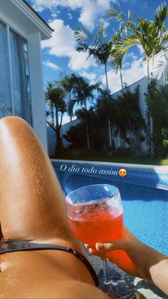 a person holding a drink in front of a swimming pool with palm trees and blue sky